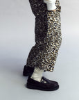 Leopard print pants worn with black shoes on a plain background