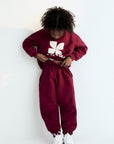 Person wearing a maroon sweatshirt and pants with a white logo on a white background