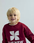 Child wearing a maroon sweatshirt with 'The New Society' logo on a light gray background