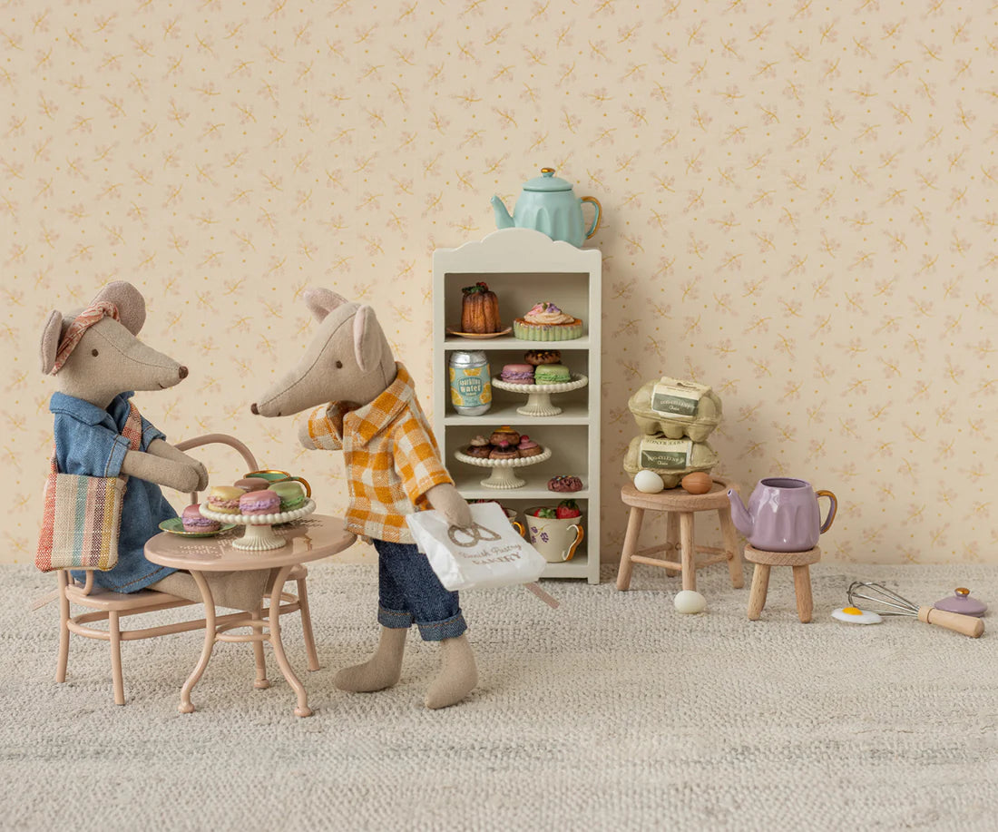Two toy mice having a tea party in a miniature room with a shelf of tea sets. Dad Mouse