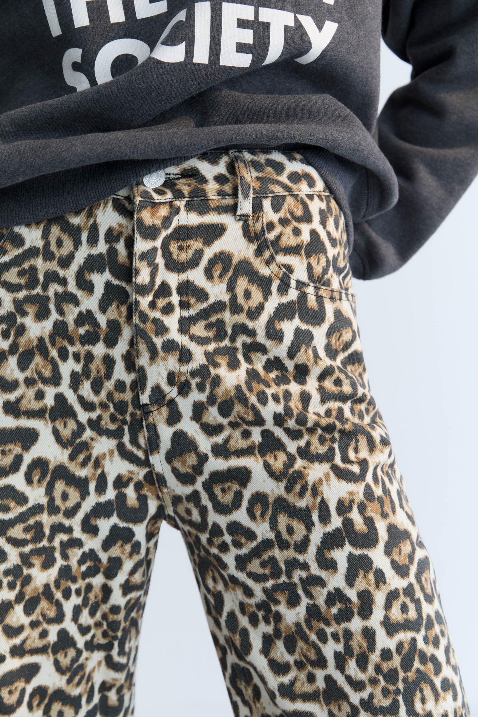 Leopard print pants worn with a dark hoodie on a light background