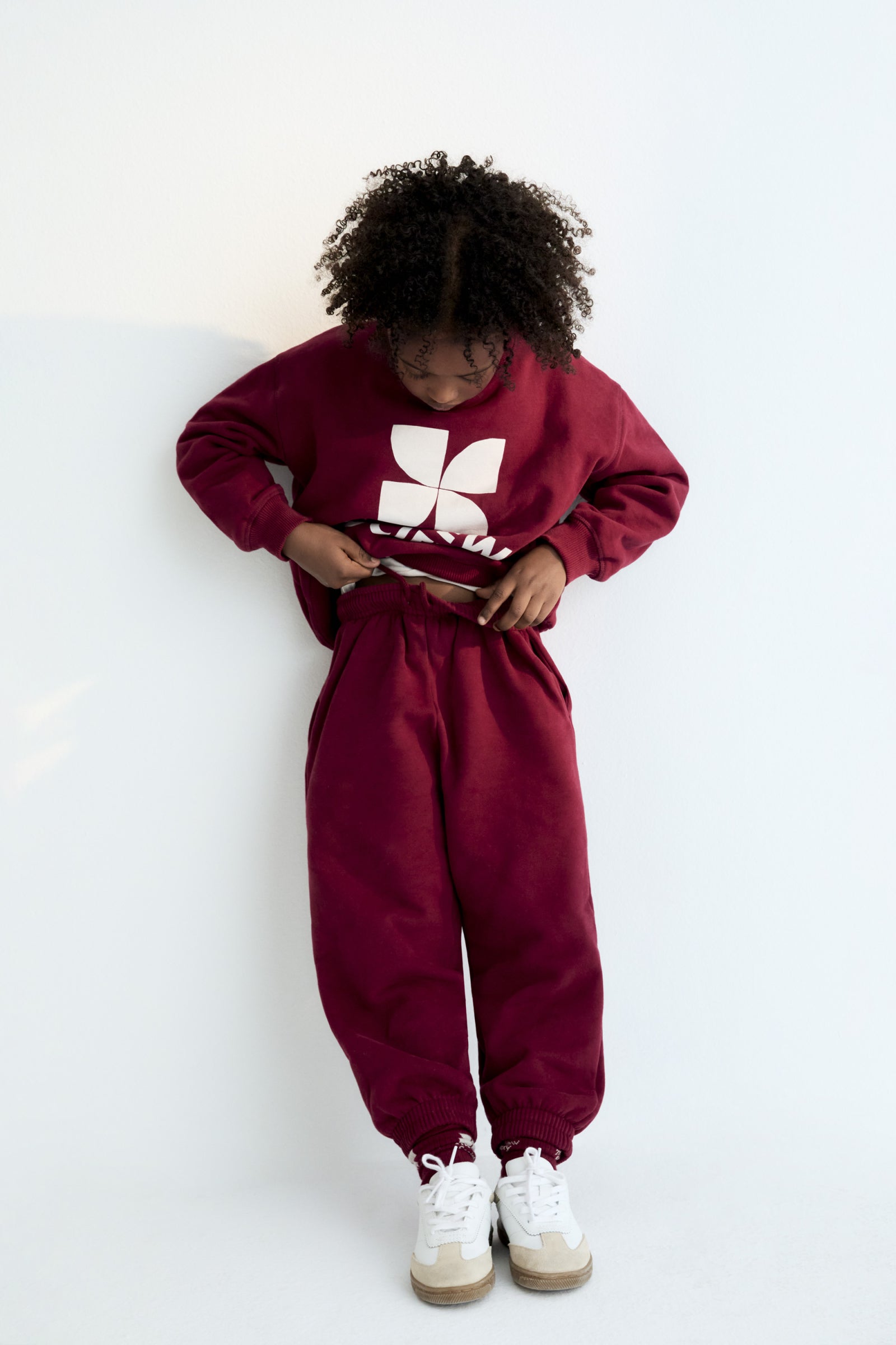 Person wearing a maroon sweatshirt and pants with a white logo on a white background